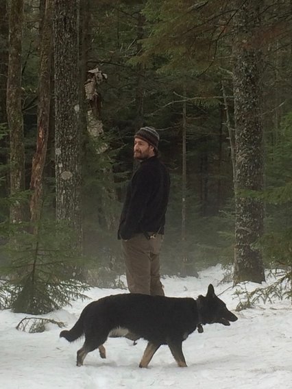 Trainer standing in woods with german shepherd